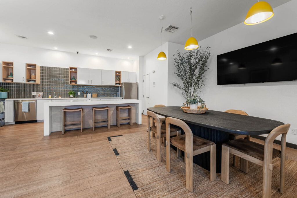 Clubhouse dining space with kitchen, dining table and chairs, wall mounted television, and bar seating.